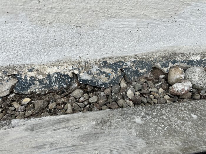 Vittrande hussockel med sprickor och mossa, stenar synliga där putsen fallit bort.