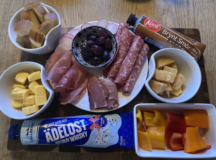 Ett urval av olika ostar och kex, skinka, salami och en tub med ädelost.