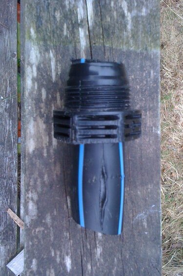 Svart plastkoppling monterad på en blå PEM-slang vilande på en träplanka.