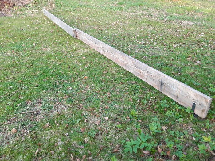 En lång träplanka med fäste på gräsmatta som avspärrning för robotgräsklippare.