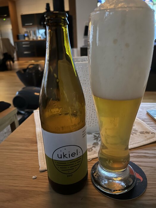 Flaska av Ukiel öl från 2017 och ett ölglas med skummande APA på ett bord.
