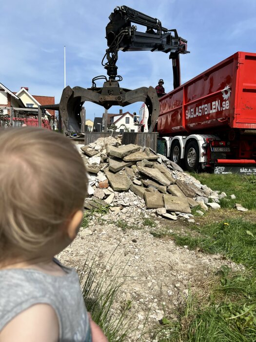 Ett litet barn tittar på en lastbil från Såglastbilen som lastar byggavfall.