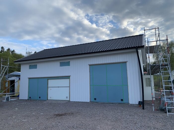 Ny målad vit garagebyggnad med svart tak och en stor och en liten port, omgivet av ställningar.