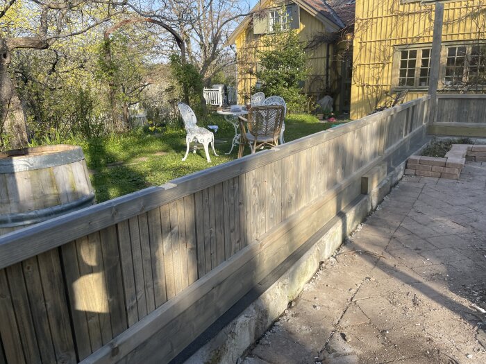 Pågående montering av växthus med hög grundbalk på mur i en trädgård, bredvid äldre gula hus.