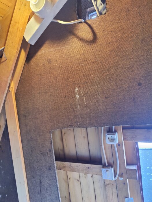En öppning i ett vindgolv som visar en liten innervägg nära en yttervägg, med synlig elinstallation.