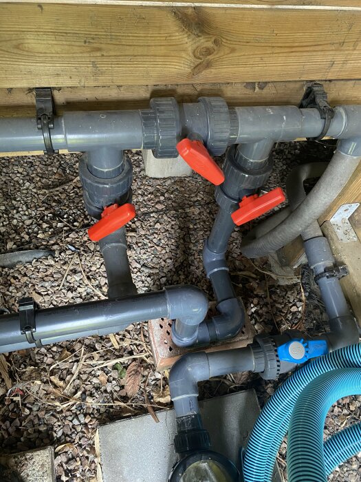 Nyligen installerat system av PVC-rör och kopplingar med röda ventiler under ett hus.