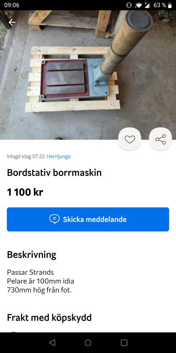 Bordstativ för borrmaskin med röd bas och en metallpelare på en träplattform mot en betonggolvbakgrund.