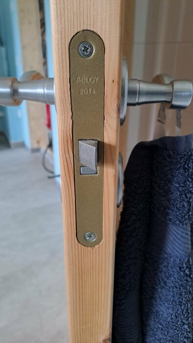 Gammal dörr med modernt toalettvred och låscylinder märkt "ABLOY 2014" monterat på träytan.