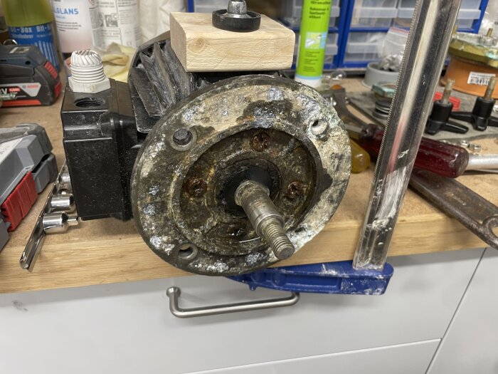 En korroderad elmotors fläns på en arbetsbänk med verktyg, visar tecken på vattenskada och slitna delar.