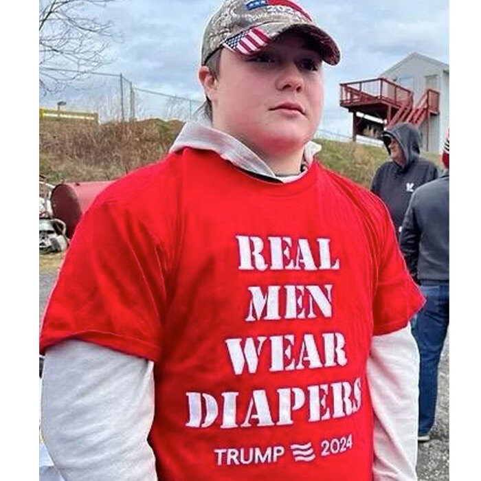 Person i röd tröja med texten "REAL MEN WEAR DIAPERS TRUMP 2024" och en keps med USA-flaggan.