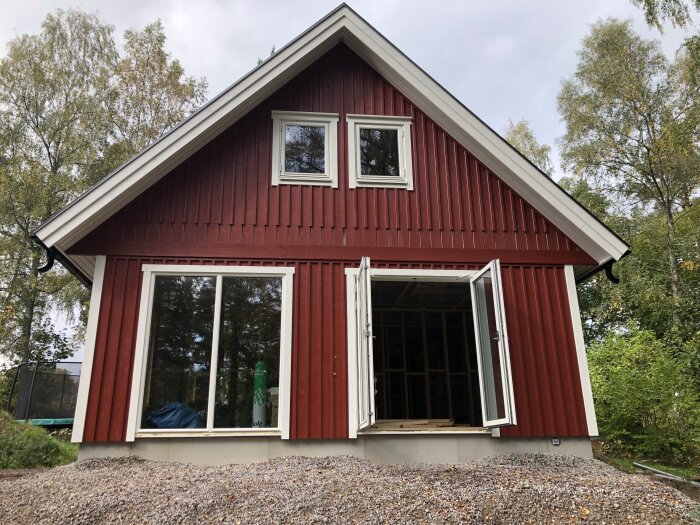 Rödmålat hus med vita fönsterkarmar och öppet fönsterlutande mot en grushög.