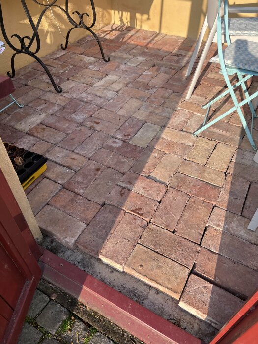 Tegelstensgolv utlagt i mönster på gjuten platta i växthus med trädgårdsredskap synligt.