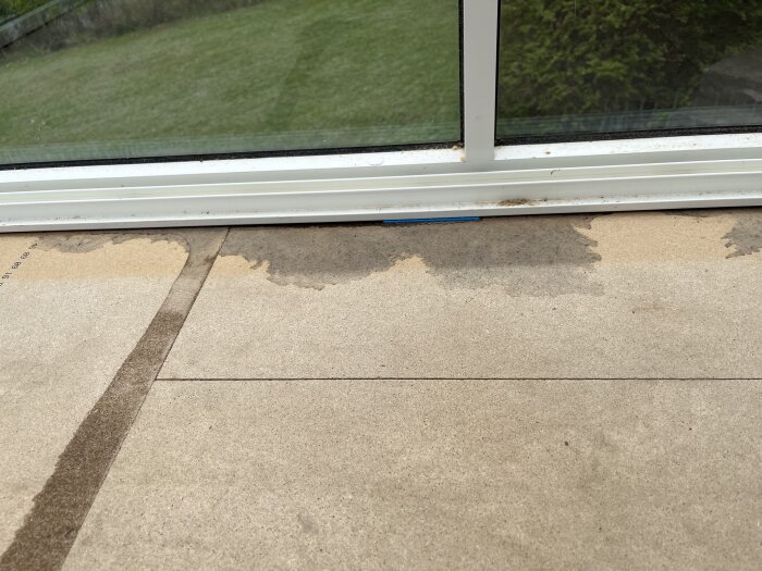 Vattenskada vid glaspartier i upprivet golv, med tydliga våta fläckar.