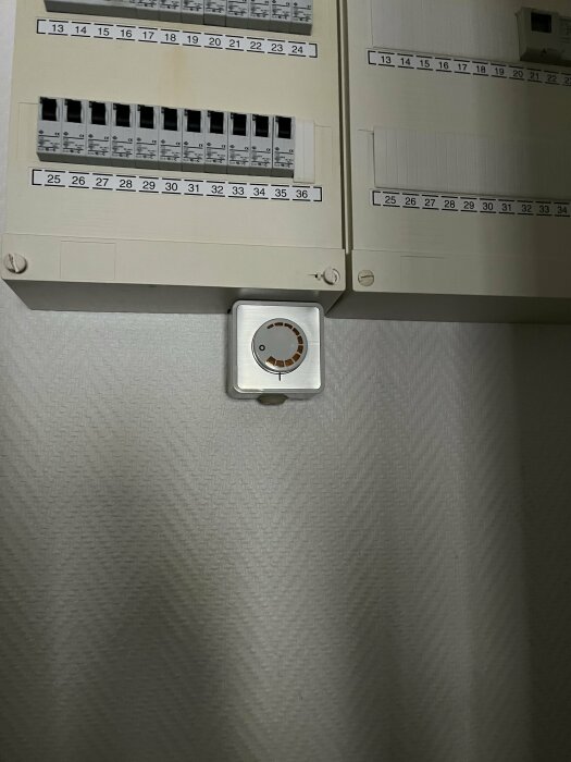 Elcentral med öppen dörr och termostat för värmeinställning på vägg.