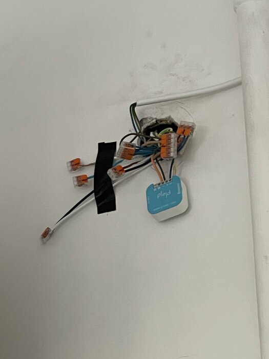 Elektriska kablar anslutna med skarvklämmor och isolerade med tejp i ett vägguttag under installation.