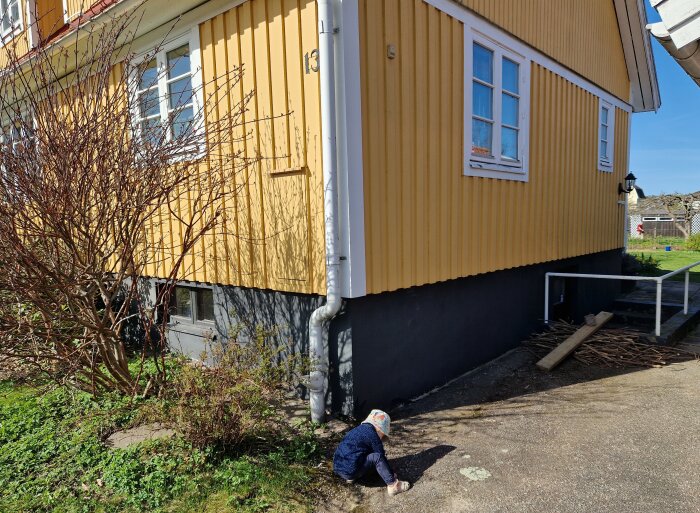 Person inspekterar en sprucken och flagad sockel på ett gult hus.
