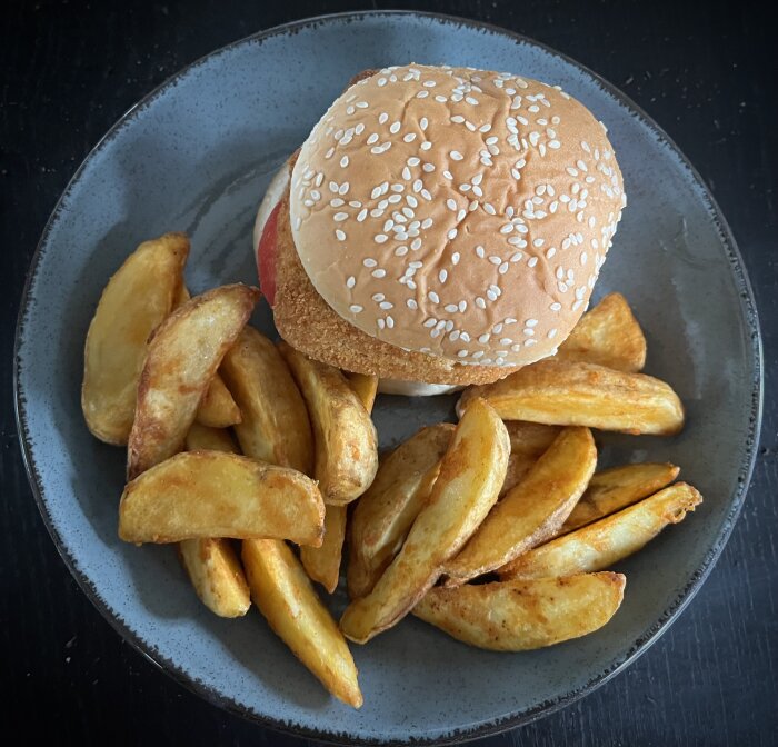 Hamburgare med sesambröd, ostfylld kalkon och kryddiga potatisklyftor på grå tallrik.