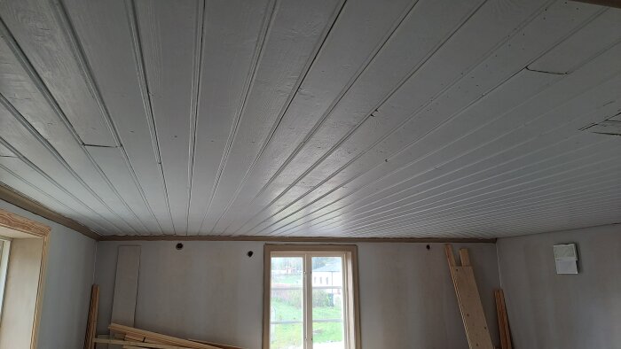 Nymålat trätak och vägg med inbyggd bänk i ett rum under renovering.