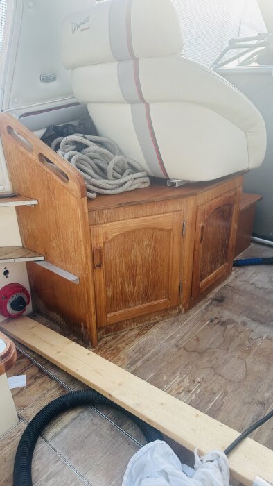 Träskåp med allmogestil och paneler ombord på en båt som ska renoveras, omgiven av verktyg och byggmaterial.