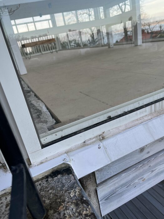 Utsikt genom en glasdörr till en veranda med skadad tröskel och tecken på slitage på tröskelns vita yta.