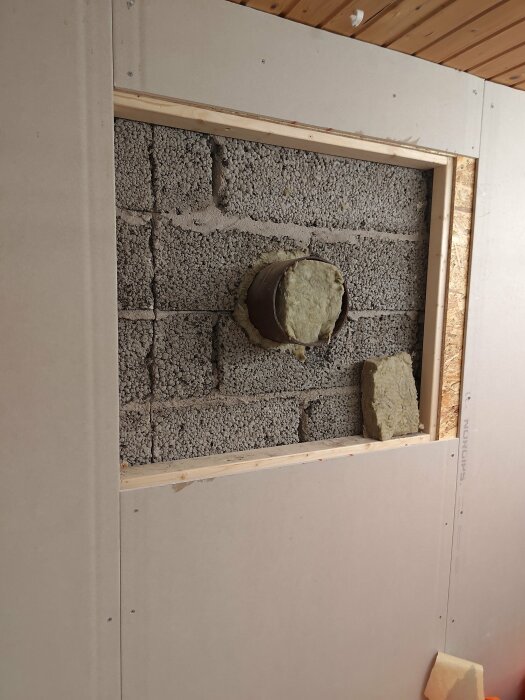 Rökrör som sticker ut från en lecavägg inramad av trä, isolering synlig, väggen förberedd för inbyggnad.