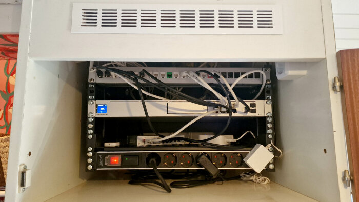 Nätverksskåp med USW-24 Pro switch, ordnade kablar och anslutna enheter, visande PoE och SFP+ DAC-kabel.