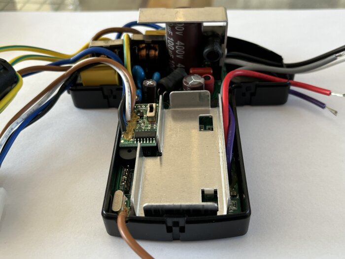 Inuti en öppen elektronikdosa med synligt kretskort och flera anslutna färgade kablar.