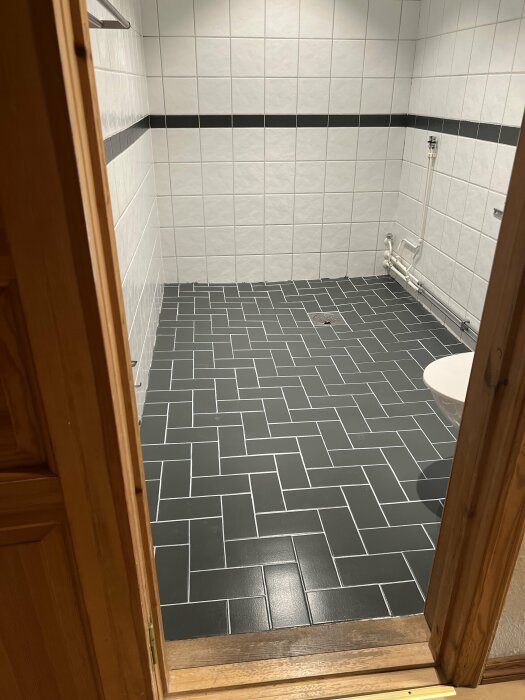 Nyrenoverat badrum med nyligen målat grått golv och vita kakelväggar med en svart bård.