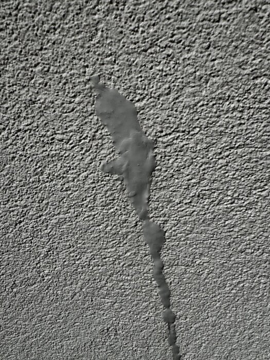 Applicering av grå mjukfog på en spricka i en grovt strukturerad vägg, vilket resulterar i en ojämn och klumpig yta.
