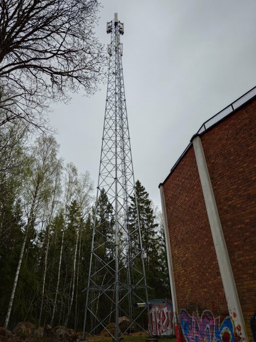 Telekommunikationstorn bredvid en byggnad med klotter, omgivet av träd.