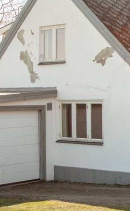 Husfasad med sprickbildning och färg som flagar nära takkanten och runt fönster.
