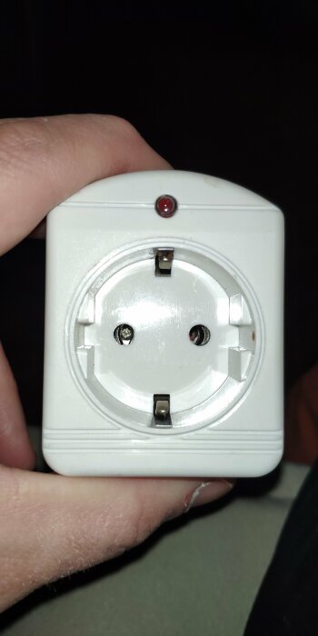 Hand håller en vit okänd enhet med elektrisk kontakt och röd lysdiod, märkt Computime.