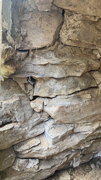 Stenmur med sprickor och lossnande stenar vid en dörrkarm, tecken på strukturella problem.