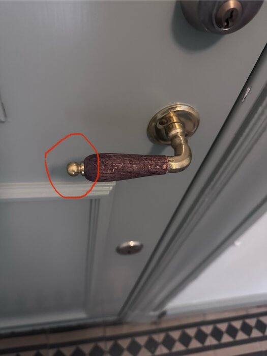 Dörrhandtag i mässing på en ytterdörr med en saknad mutter framhävd med en röd cirkel.