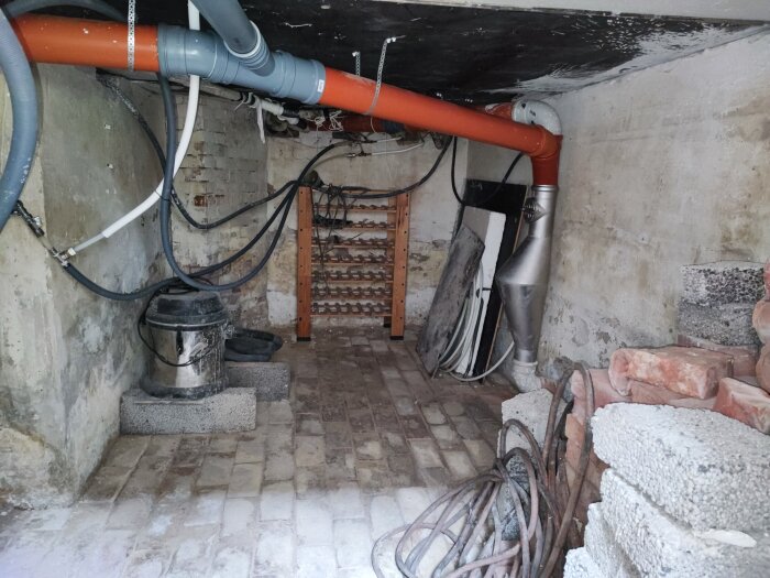 Nyinstallerade rörledningar i en källare med synliga tegelväggar, kablar och gammal utrustning.