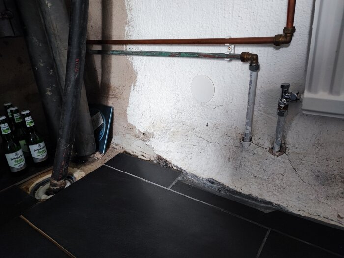 Vattenledningar i källare med synliga gamla och nya rör nära väggen och golvet.