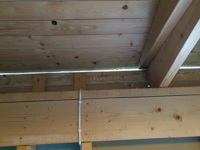 Oisolerad skarv mellan tak och vägg med synliga träbjälkar och en vit PVC-rörinstallation i ett framtida förråd.