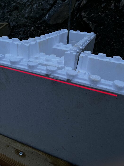 Första lagret av vita byggblock på en grå betongplatta med en röd laserlinje som visar höjdskillnader.