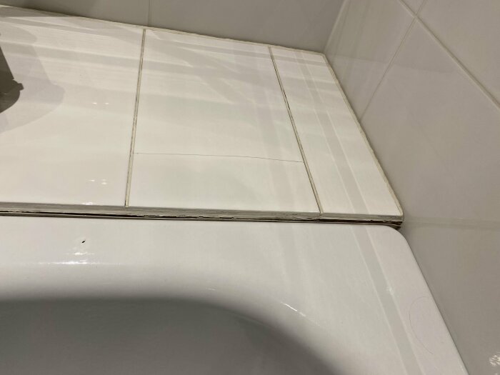 Kantlist som släppt på vit kakelhylla bredvid badkar i ett våtrum.