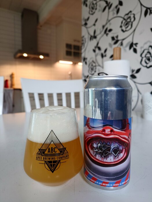 Öl från Apex Brewing i glas och burk mot bakgrund av ett kök och blommigt tapet.