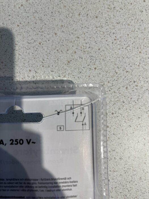 Elkopplingsschema på förpackning med knapp och brytare i solljus.