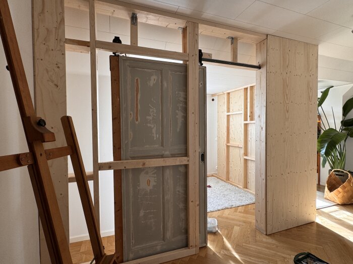 Byggprocess av ett extrarum med träreglar och konstruktionsplywood som väggbeklädnad, synlig ramstruktur.