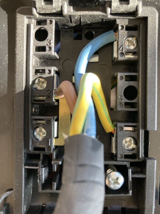 Närbild på en elektrisk inkopplingsplint med tre kablar i blått, brunt och gult/grönt anslutna, för installation av häll.