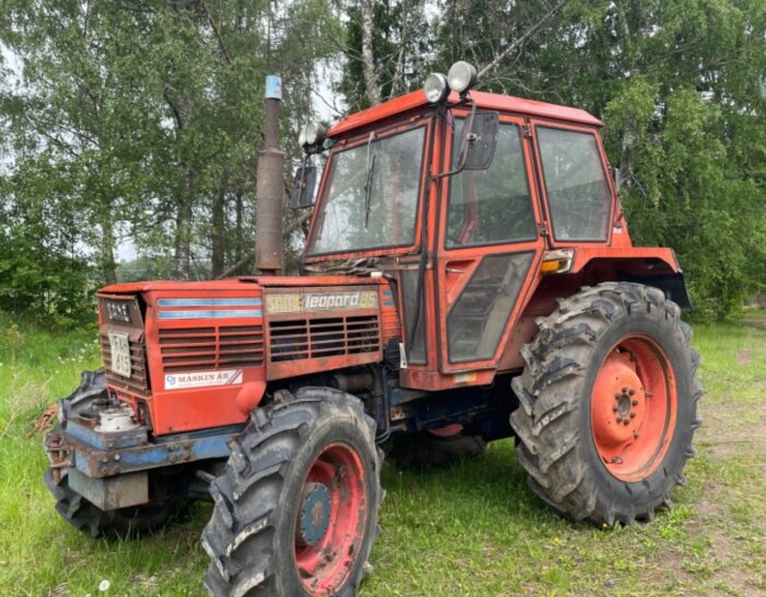 Röd Same Leopard 85 traktor parkerad utomhus med slitage och grönska i bakgrunden.