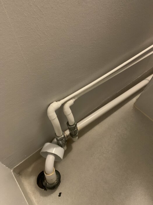 Vattenledningsrör som kommer upp ur golvet i ett hörn av ett rum.