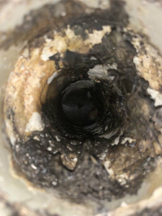 Närbild på ett igentäppt svart rör med synliga avlagringar och smuts.