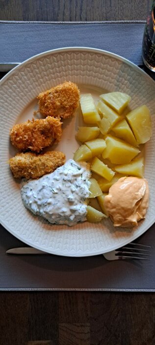Tallrik med fiskfrilletter av alaskisk pollock, kokt potatis, vit sås med dill och majonäs.