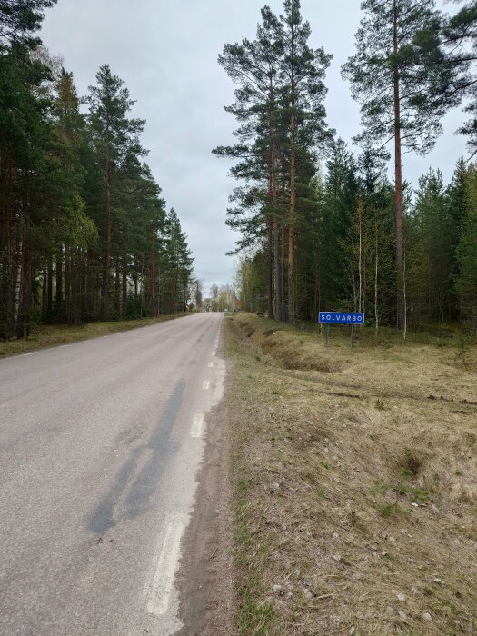 Asfalterad landsväg omgiven av barrskog med skylt för orten Sölvabäck.