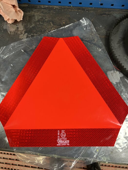 Röd reflekterande säkerhetstriangel för fordon med E-märkning och tillverkares logotyp.