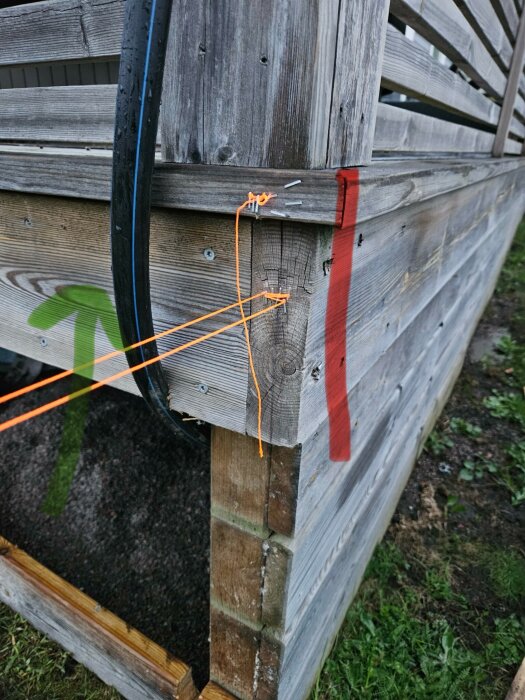 Trästolpe med markerad röd såglinje och orange linjer med grön pil som instruktioner.
